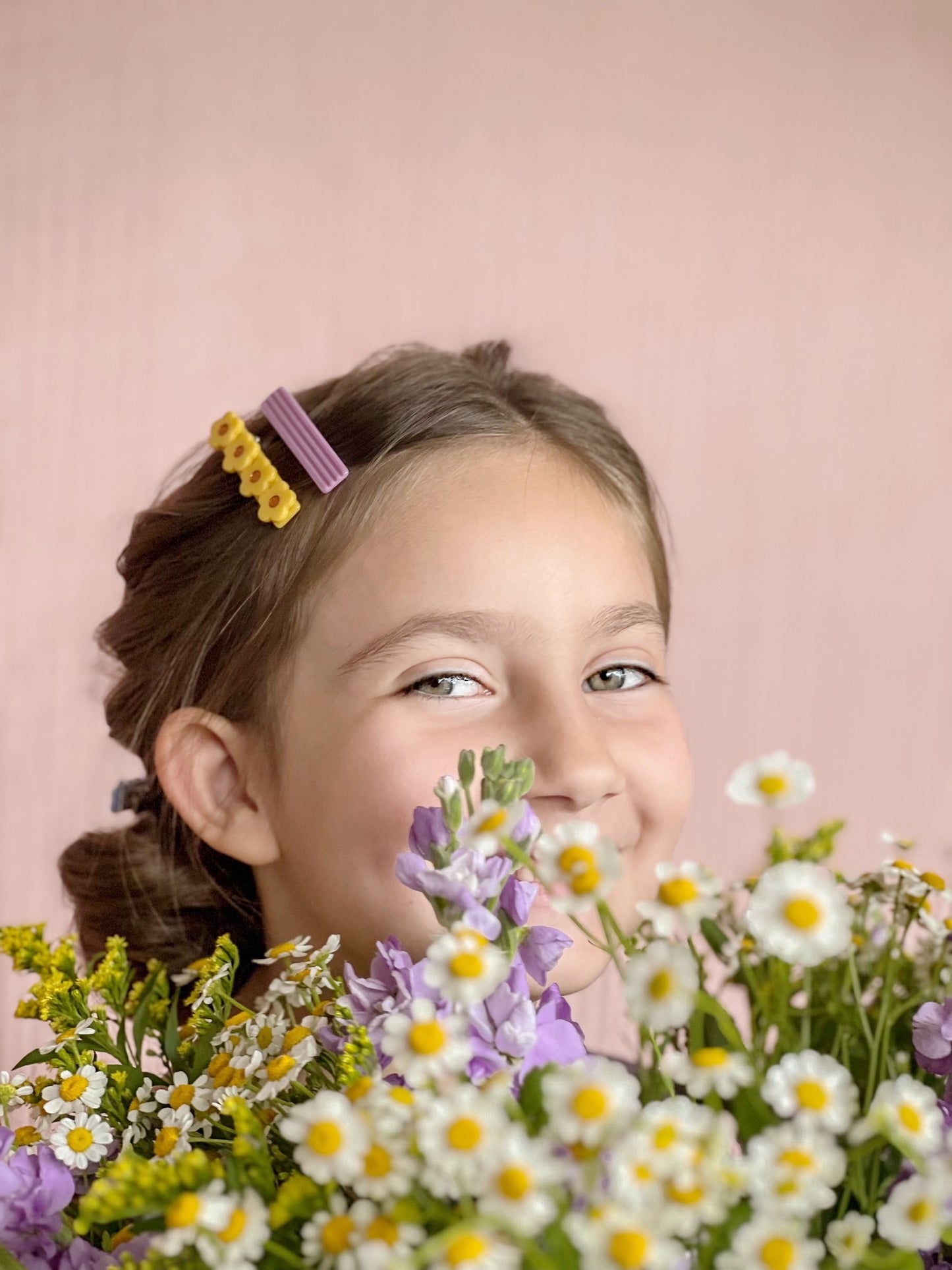 yellow and lilac hair barrettes in a low bun hairstyle for girls. cute summer or spring picture idea with wildflowers.